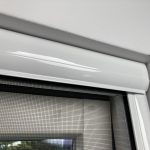 Baltā loga rāmis ar sieta sietu, kas novietots pie baltas sienas, tuvplānā.