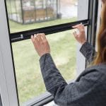 Henkilö liukuu ylös Hyttysverkko ikkunaan - rullaverkko, josta paljastuu ruoho ja ulkorakennus ulkona.