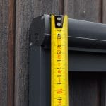 Mittanauhaa pidetään pystysuorassa Hyttysverkko ikkunaan - rullaverkko kehystä vasten puuseinässä sen korkeuden mittaamiseksi.