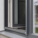 Lähikuva modernista ikkunasta, jossa on metallikehys ja Hyttysverkko ikkunaan - rullaverkko, jossa näkyy sarana ja seinän yksityiskohta.