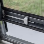 Lähikuva Hyttysverkko ikkunaan - rullaverkko harmaalla salvalla, mustalla sääsuojalla ja lisätyllä hyönteissuojalla.