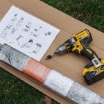 Hyttysverkko ikkunaan - rullaverkko, kääritty metalliosa ja ohjeet sijoitettu pahville ruohon päälle.