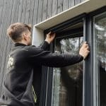 Mies asentaa Hyttysverkko ikkunaan - rullaverkkoa pystypuuvuoratun rakennuksen ikkunaan.