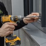 Henkilö asentaa DeWalt-akkuporakoneella Hyttysverkko ikkunaan - rullaverkko metalliikkunaan.