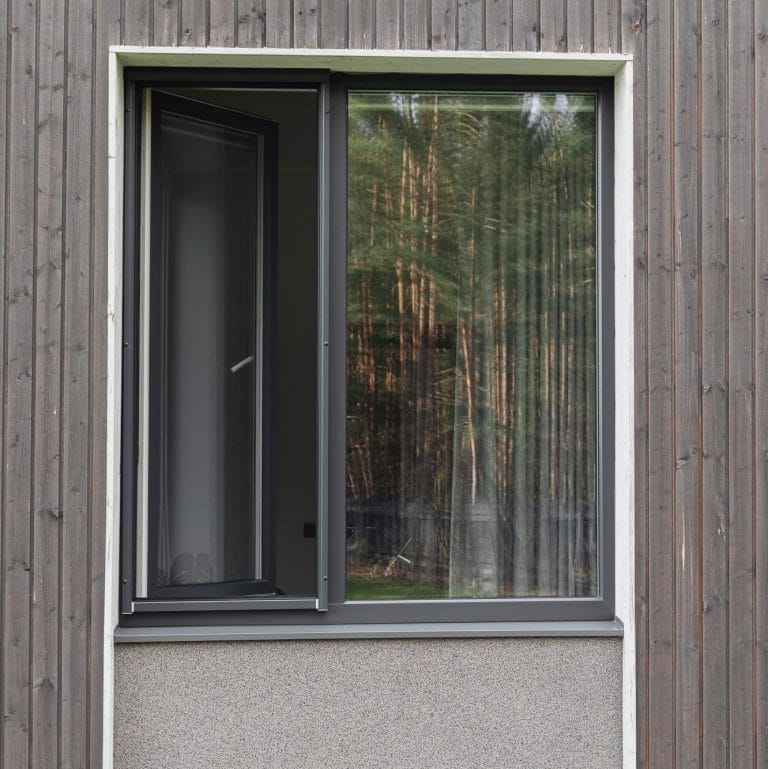 A modern Insect screen window – roller blind on a wooden wall, with trees softly reflected in the glass.