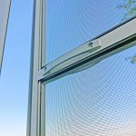 Close-up of Insect screen door - hinged with a white handle, set against a clear blue sky background.