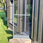 Stikla vētras durvis un Insektu siets durvīm - verams ir atvērtas uz mājas ar vertikālu koka apšuvumu, kas vērsts uz zālāju klātu pagalmu.