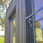 Lähikuva Hyttysverkko oveen - avattava puinen ulko-ovi, lasi-ikkunassa heijastuvat puut.