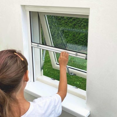 Bērns baltā krekliņā atver logu, skatoties garām Insektu siets logiem - rullo zaļā zālē un krūmos.