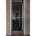 En Myggnät dörr - öppningsbar med en mörk metallram är placerad i en trävägg och visar det inre rummet genom sitt glas.