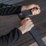 Henkilö kokoaa puulattialla kahta Hyttysverkko oveen - taitettava metallista runkopalaa, yksi osa kummassakin kädessä.