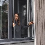 Nainen sisätiloissa irrottaa Hyttysverkko ikkunaan - kehysmallia avoimesta ikkunasta.
