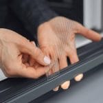 Henkilön käsi vetää kielekkeestä liu'uttaa Hyttysverkko ikkunaan - kehysmalli ikkunan auki.